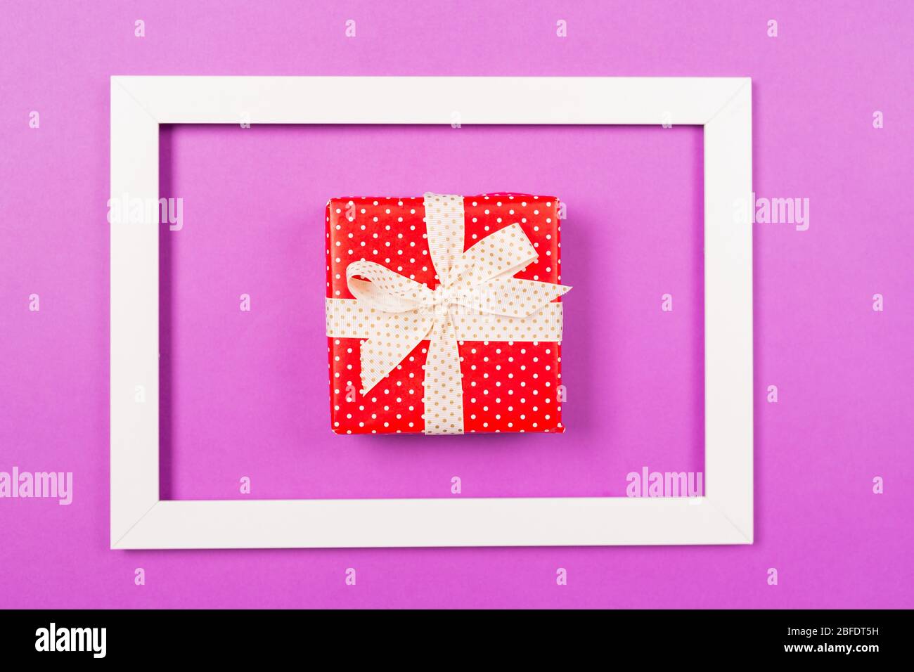 Rote Geschenkbox im Rahmen auf lila Hintergrund. Konzept zum Valentinstag-Geburtstag der Mütter. Vorlage für den Boxtag. Kopierbereich. Platz für Text Stockfoto