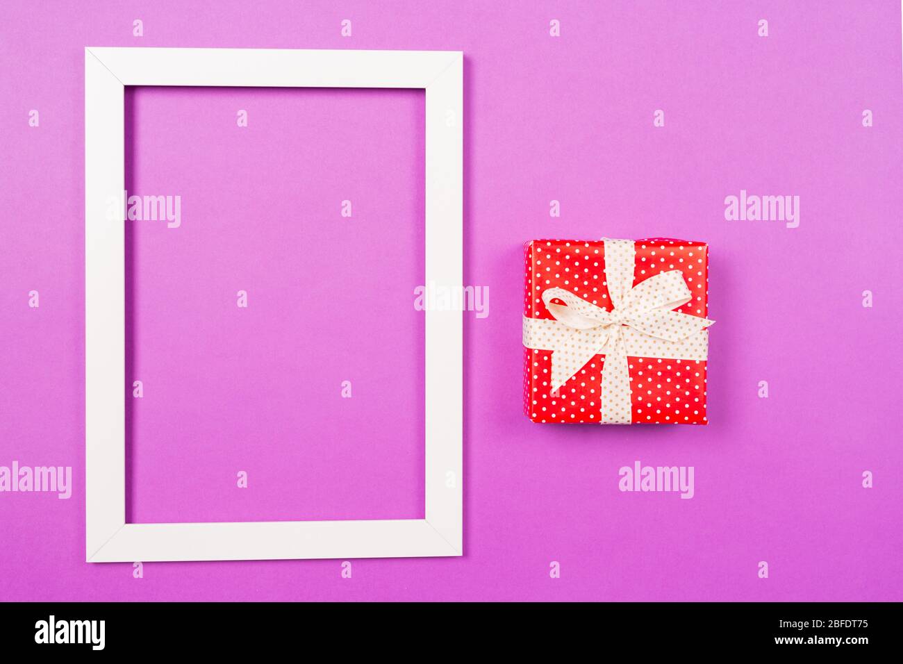 Rote Geschenkbox und weißer Bilderrahmen auf lila Hintergrund. Konzept zum Valentinstag-Geburtstag der Mütter. Vorlage für den Boxtag. Kopierbereich Stockfoto
