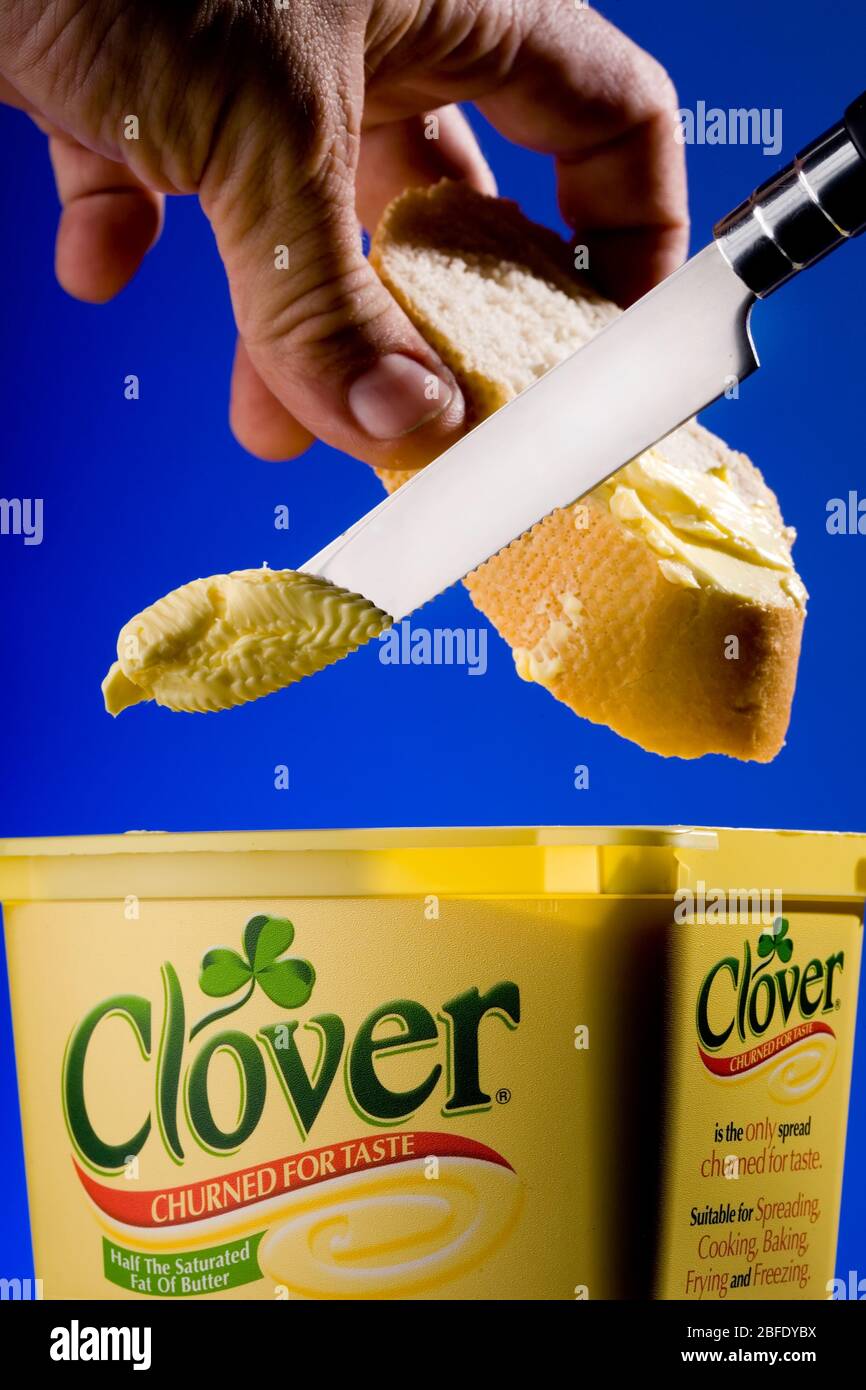 Das Bild zeigt Kleebutter, Produkte von Dairy Crest mit einem Messer und einen Mann, der eine Scheibe Baguette hält Stockfoto