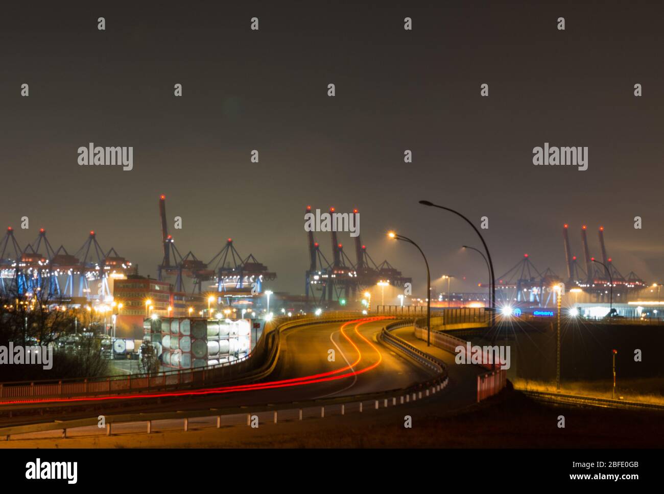 Lange Belichtung bei Nacht mit Blick auf die Autostraße und Lichtstrahlen von vorbeifahrenden Autos, die in den Industriehafen und Hafenbereich von Hamb führen Stockfoto