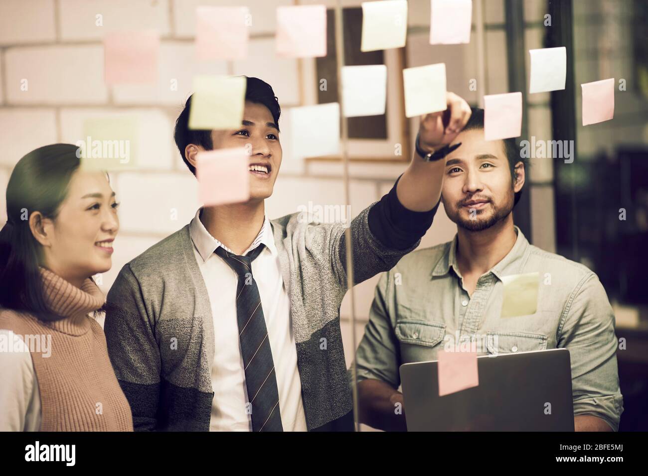 Drei asiatische Kleinunternehmer junge Unternehmer, die mit Haftnotizen im Büro diskutieren Stockfoto