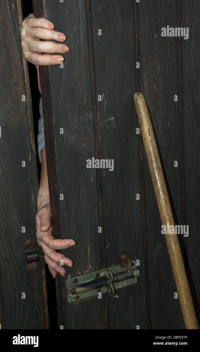 Kaukasische Hände ragen hinter einer alten und verwitterten Holztür hervor, die geschlossen gehalten wurde und ein Besen versuchte, dem Verschließen zu entgehen Stockfoto