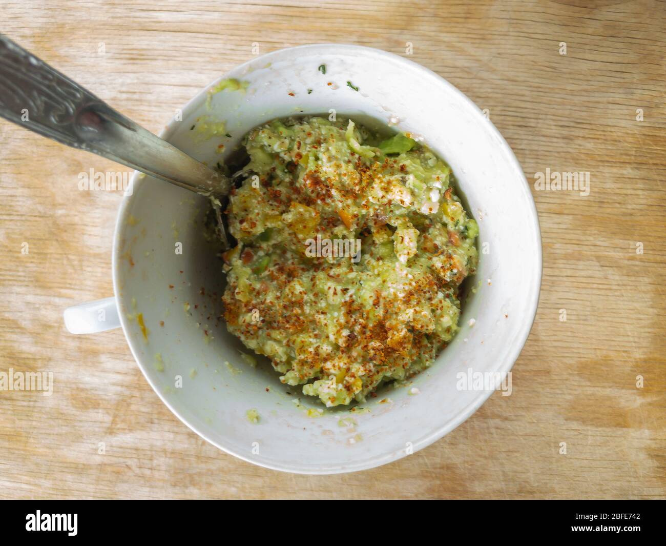 Draufsicht auf kleine Tasse mit handgefertigten Guacamole-Aufstrich gefüllt mit geriebenen und getrockneten Avocado-Stein gewürzt Stockfoto