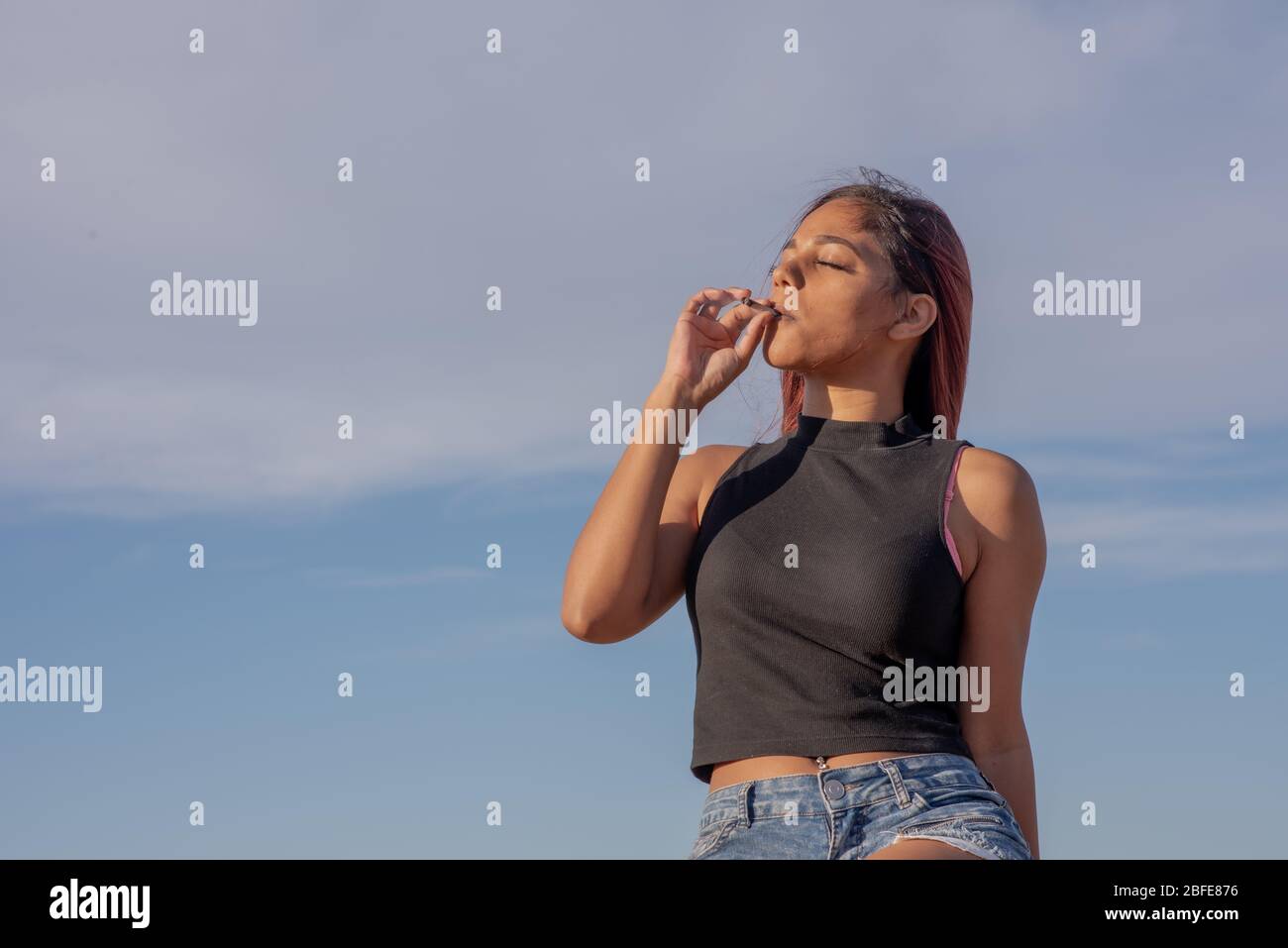 Port Elizabeth, Südafrika April 2020 Junge Frau, die Marihuana gegen klaren blauen Himmel raucht Stockfoto