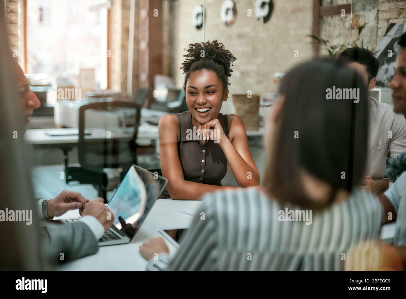 Wir sind ein Team! Junge und fröhliche Afro-amerikanerin lächelnd, während sie ein Treffen mit Kollegen im modernen Büro hat. Geschäftskonzept Stockfoto