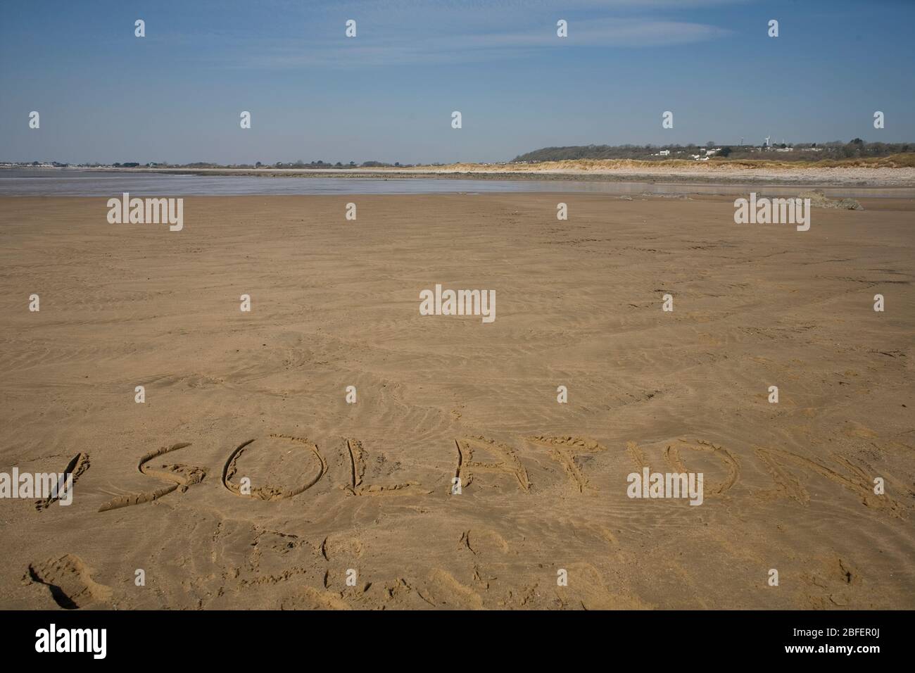Das Wort Isolation schrieb sich in den frühen Tagen der pandemischen Sperrung auf dem Sand des Newton Beach jenseits der Black Rocks ein Stockfoto