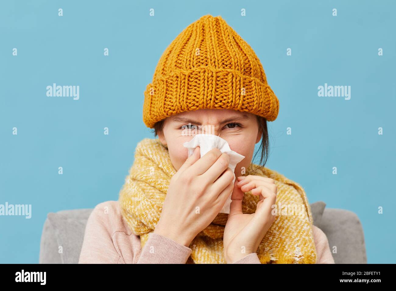 Portrait der jungen Frau in Wollmütze und Schal hat eine laufende Nase isoliert auf blauem Hintergrund Stockfoto