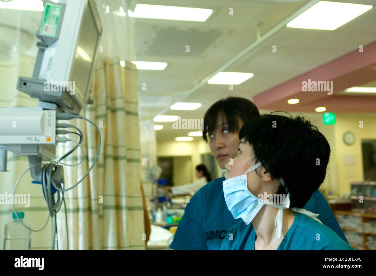Zwei medizinische Mitarbeiter untersuchen die Herzfrequenz eines Patienten auf einer Intensivstation auf einem Monitor. Stockfoto