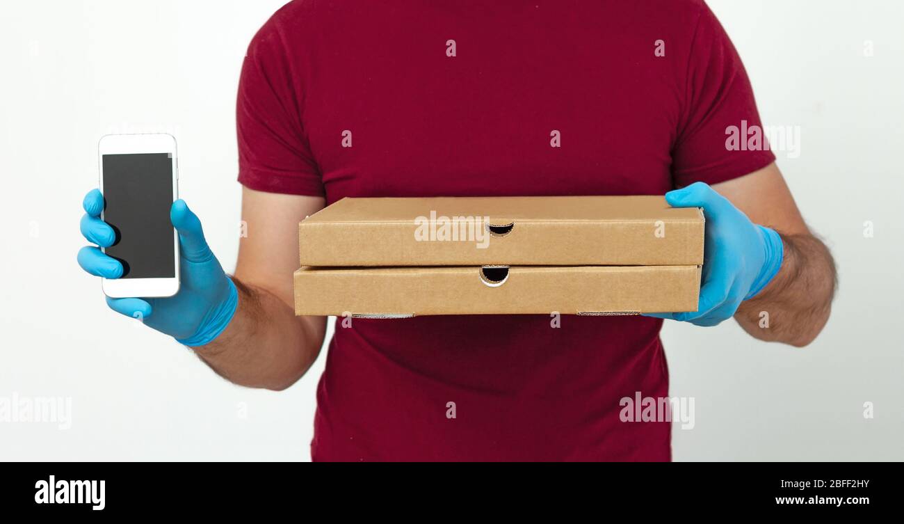 Pizzalieferung während der Quarantäne. Ein Kurier in medizinischen Handschuhen und Telefon in der Hand hält Pizzakartons. Kontaktlose Lieferung Stockfoto