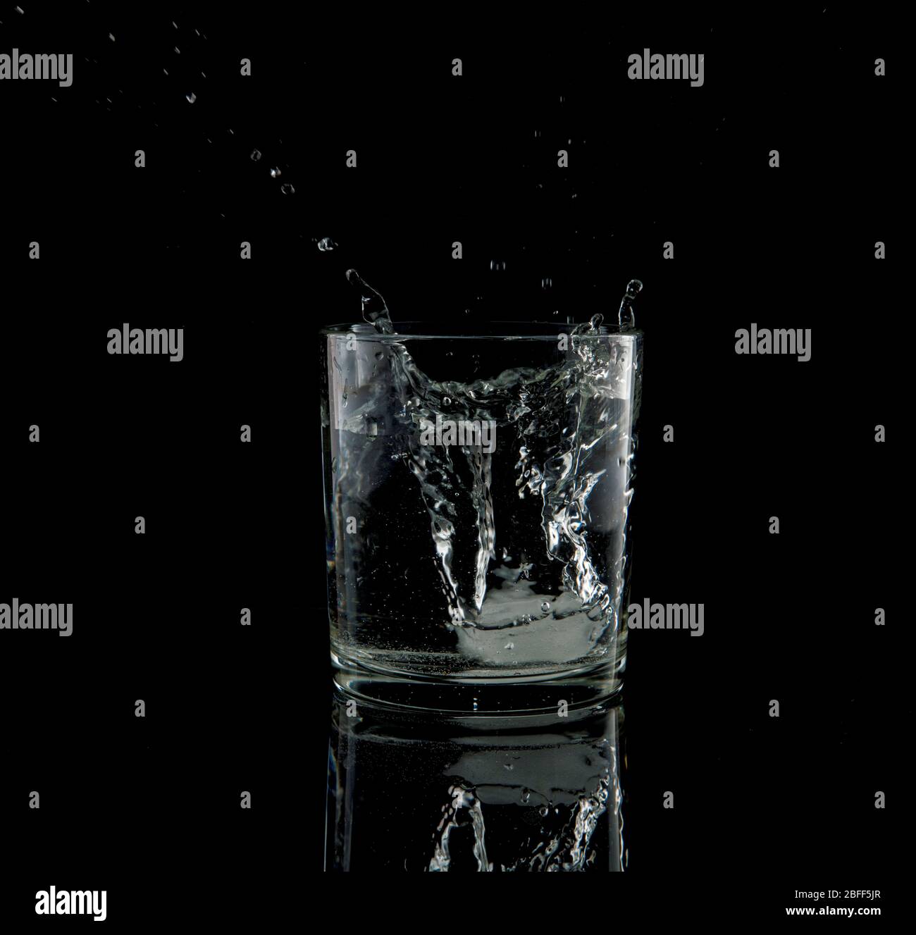 Fast schwarz-weiß von einem Spritzer aus einem fallenden Eiswürfel in Glas Wasser Stockfoto