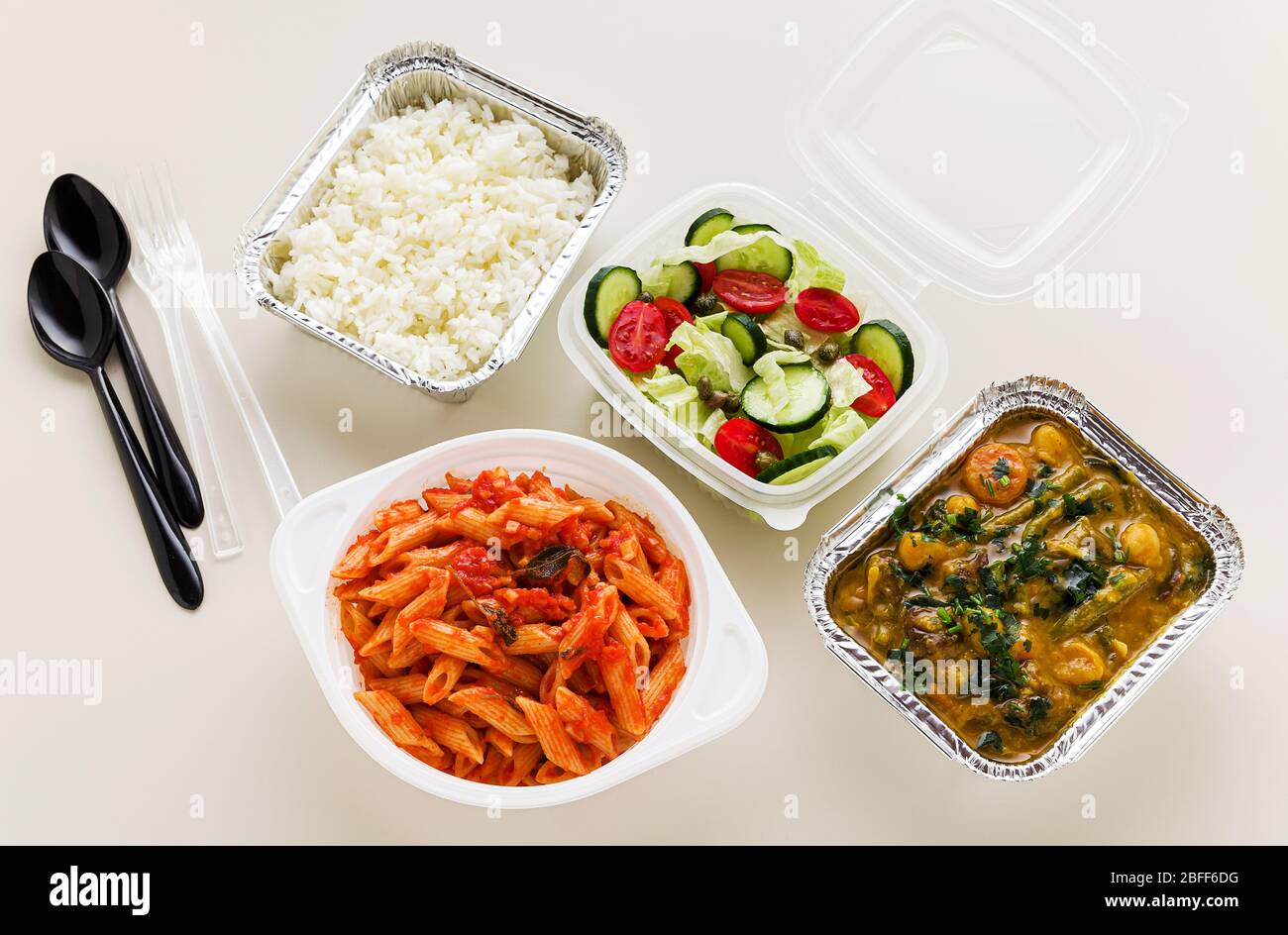 Essen zum Mitnehmen in Einwegbehältern: Reis, Gemüsecurry, italienische Pasta mit Tomatensauce und frischer gesunder Salat. Stockfoto