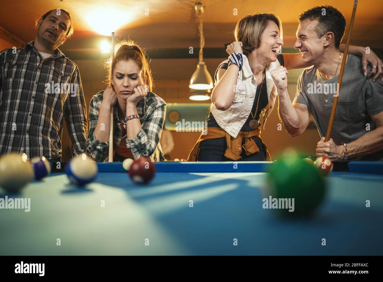 Junge, fröhliche Freunde spielen nach der Arbeit Billard in der Bar. Ein Paar, das Ruhm gewinnt und die Verlierer sind in einer schlechten Stimmung. Stockfoto