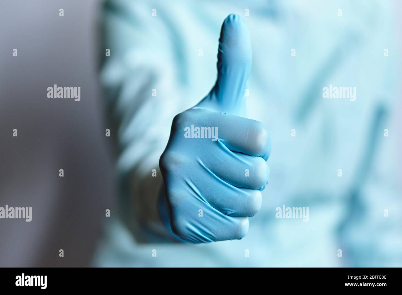 Arzt in einem Morgenmantel und medizinischen Handschuhen zeigt Daumen nach oben. Nahaufnahme. Stockfoto
