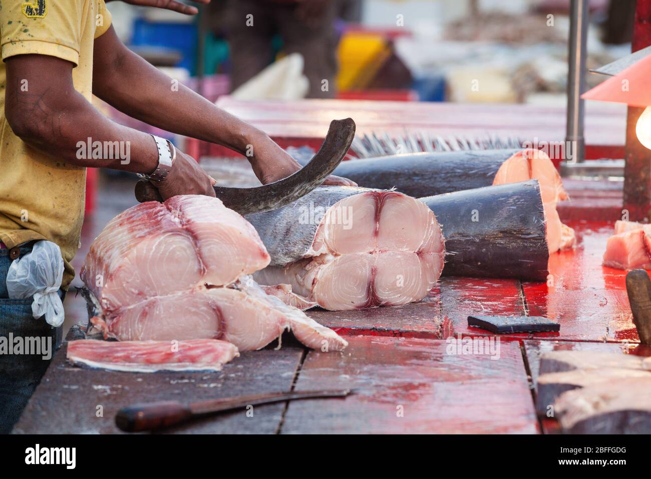 Hände mit Messer hacken Fische im Freien. Ein Fischer und Fischverkäufer verfolgt einen großen Fisch auf einem Holztisch in Scheiben geschnitten. Blut auf dem Holztisch vergossen. Stockfoto