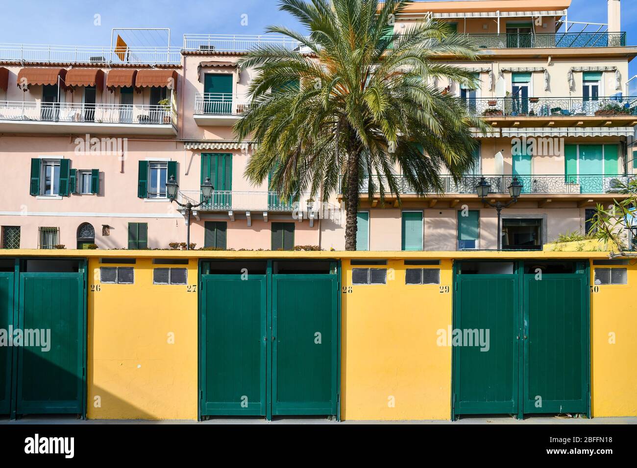 Blick auf die Uferpromenade von Sanremo mit einer Reihe von Strandhütten, einer Palme und einem Wohngebäude in hellen Farben, Imperia, Ligurien, Italien Stockfoto