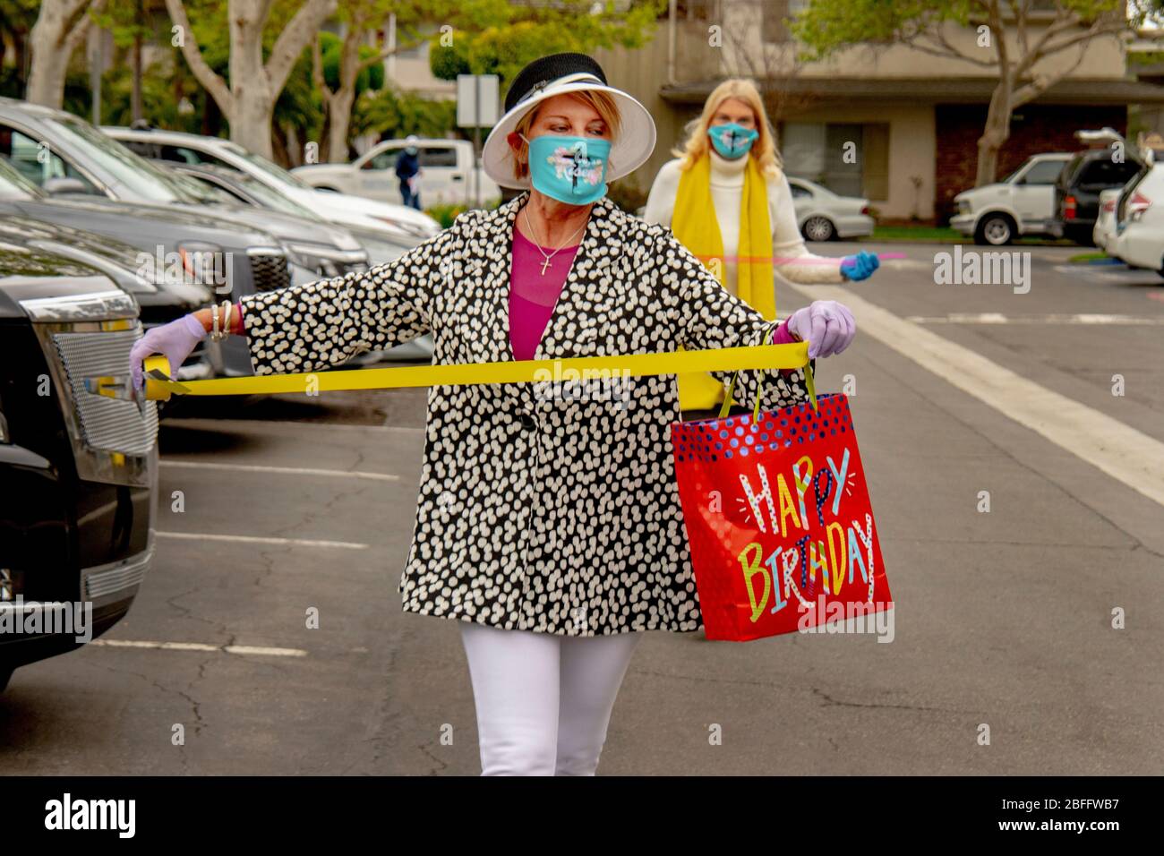 Freiwillige tragen wegen des Ausbruchs des Coronavirus oder COVID-19 eine Sicherheitsmaske, während sie ankommende Autos bei einem Drive-in-Osterdienst in einem Büropark in Santa Ana, CA, mit Bändern schmücken. Stockfoto