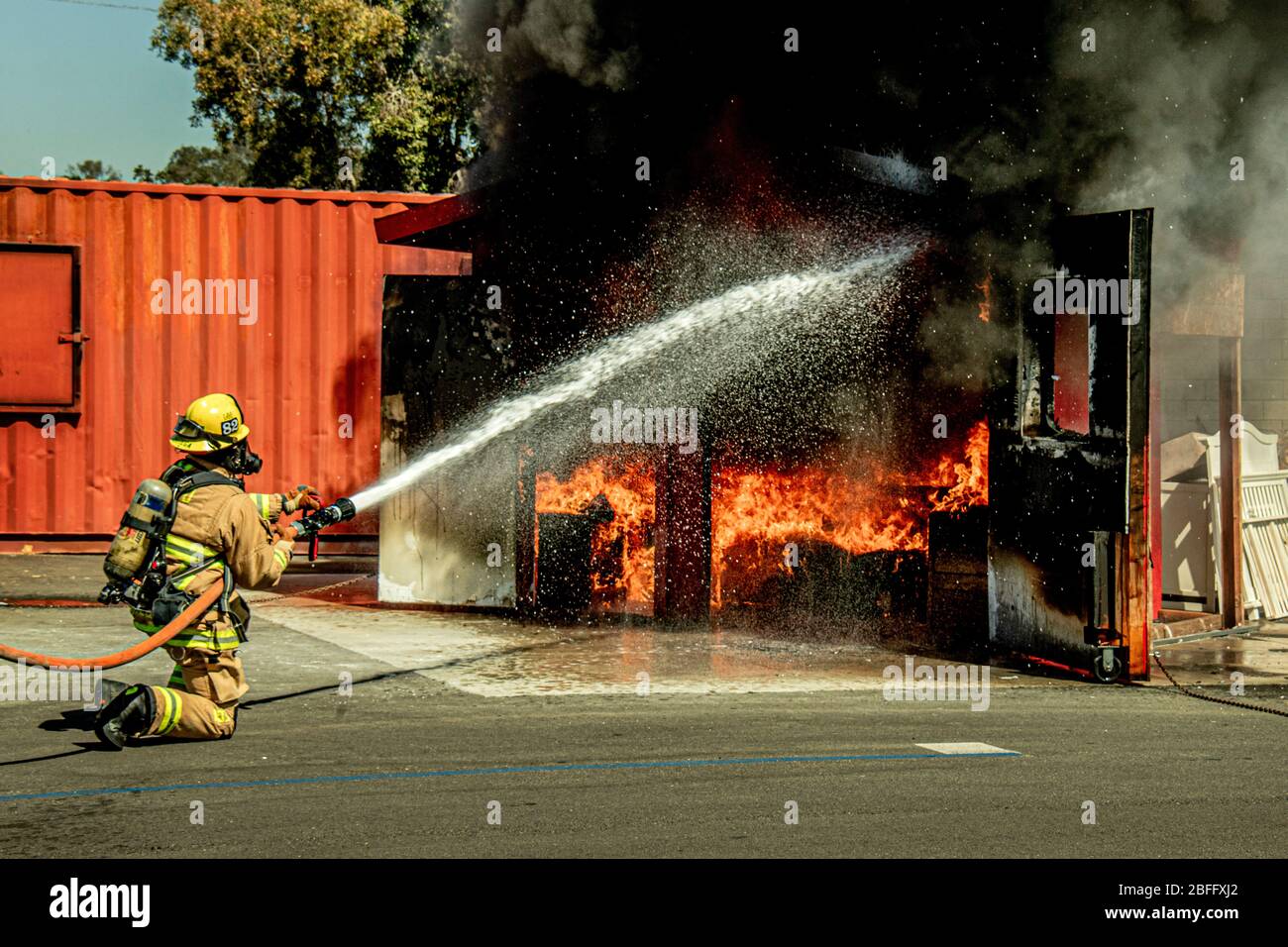 Ein Feuerwehrmann sprüht Wasser auf ein brennendes Modell Wohnzimmer in einer Feuerwehr strukturelle Brandbekämpfung Demonstration in Costa Mesa, CA. Stockfoto