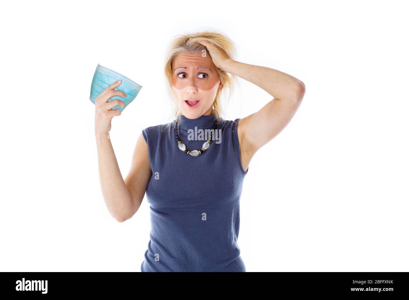 Sonnenbräune während COVID-19: Frau mit weißem Gesicht für chirurgische Maske auf weißem Hintergrund isoliert. Kaukasische blonde Frau zeigt ihre Bräune nach Quarantäne Stockfoto