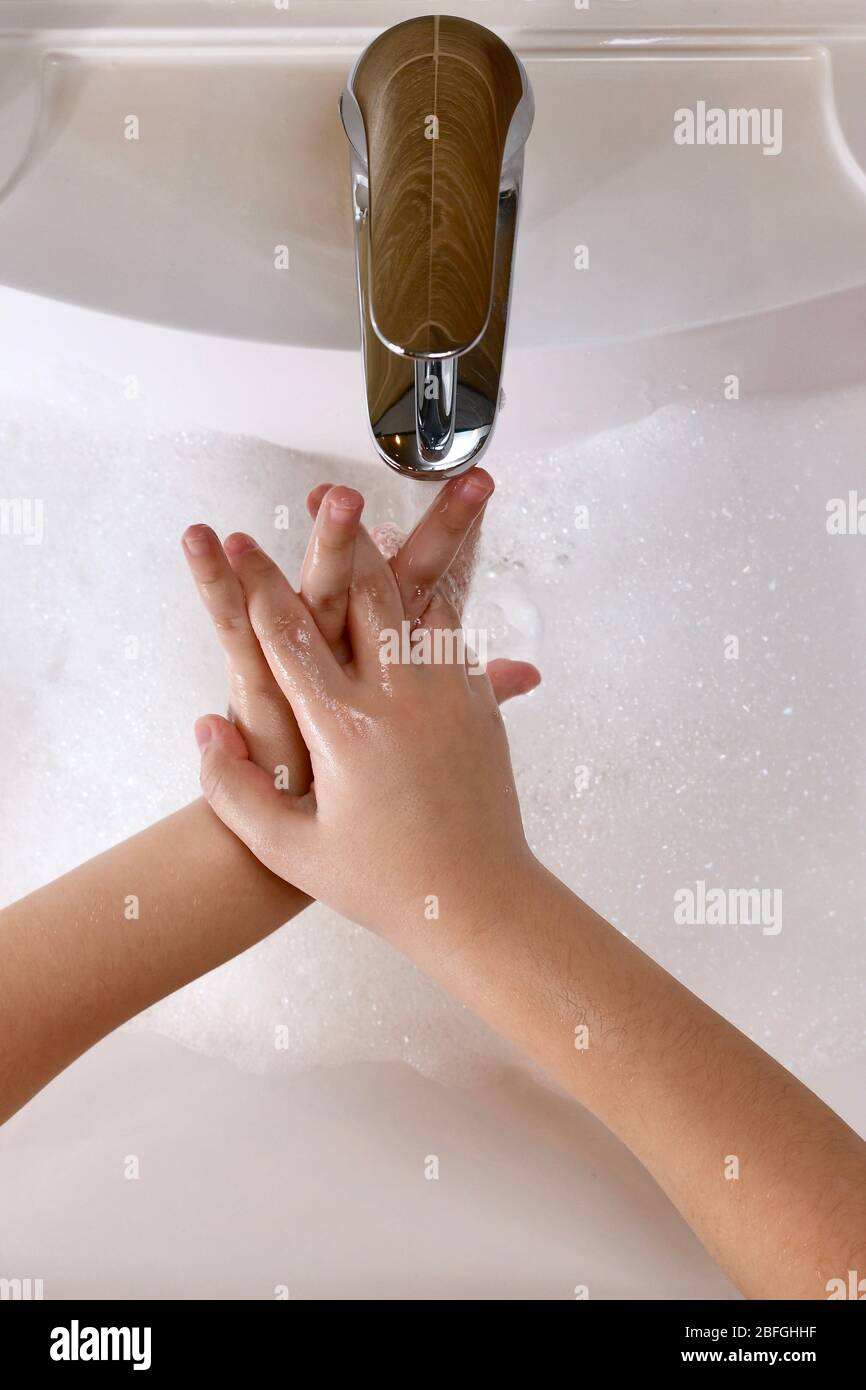 Das Kind lernt, die Außenseite der Hände zwischen den Fingern mit Wasser im Waschbecken zu waschen. Stockfoto