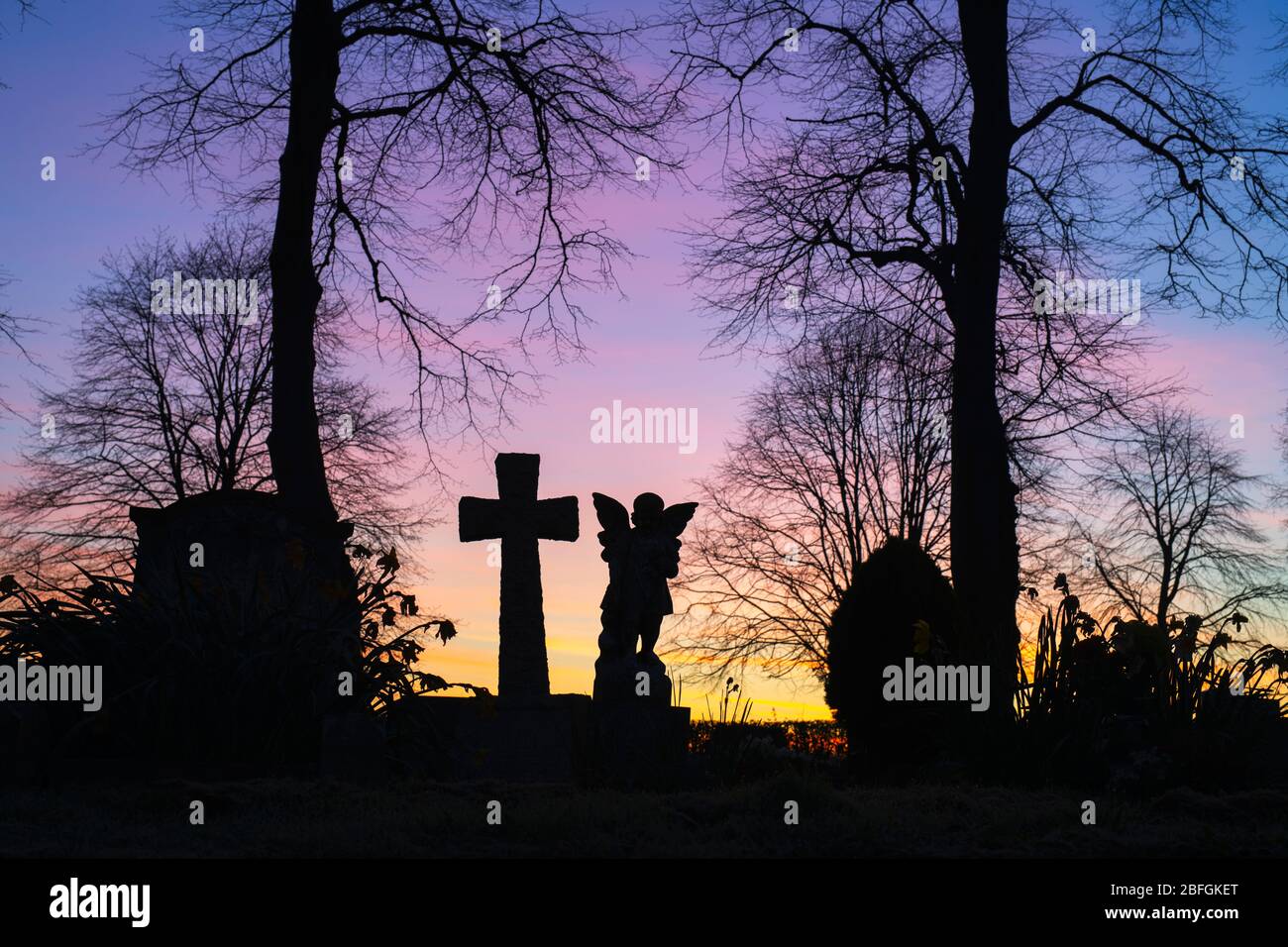 Die Silhouette des Engels und des Kreuzkopfes mit den Bäumen im Friedhof in der Morgendämmerung. Kings Sutton, Northamptonshire, England. Silhouette Stockfoto