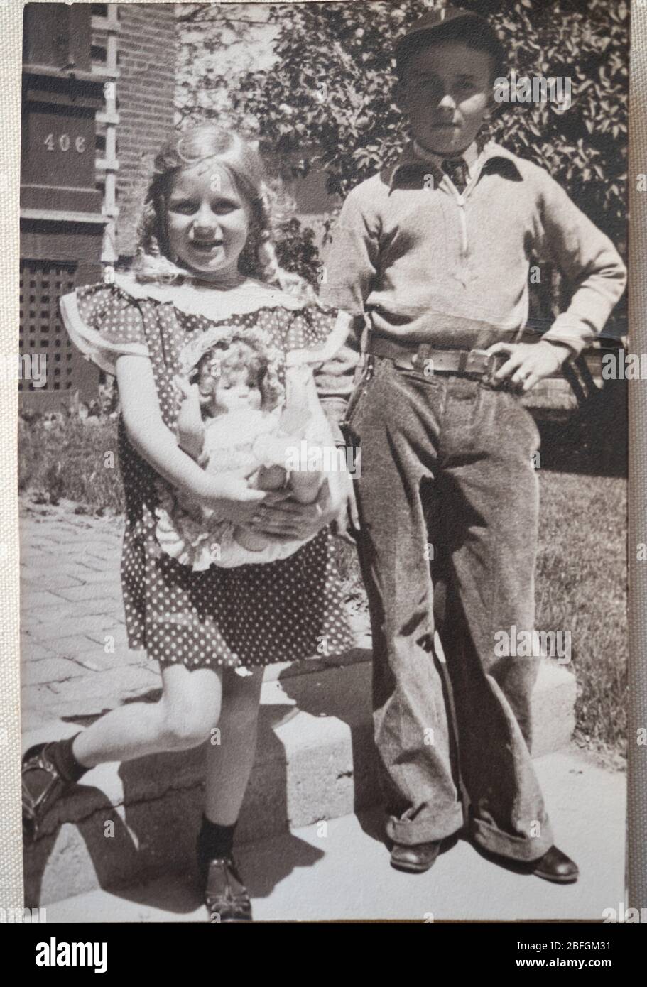 Vintage schwarz-weiß Foto von einem Bruder und Schwester mit dem Mädchen, das Puppe hält und ein Kleid mit einem Tupfen trägt. Stockfoto