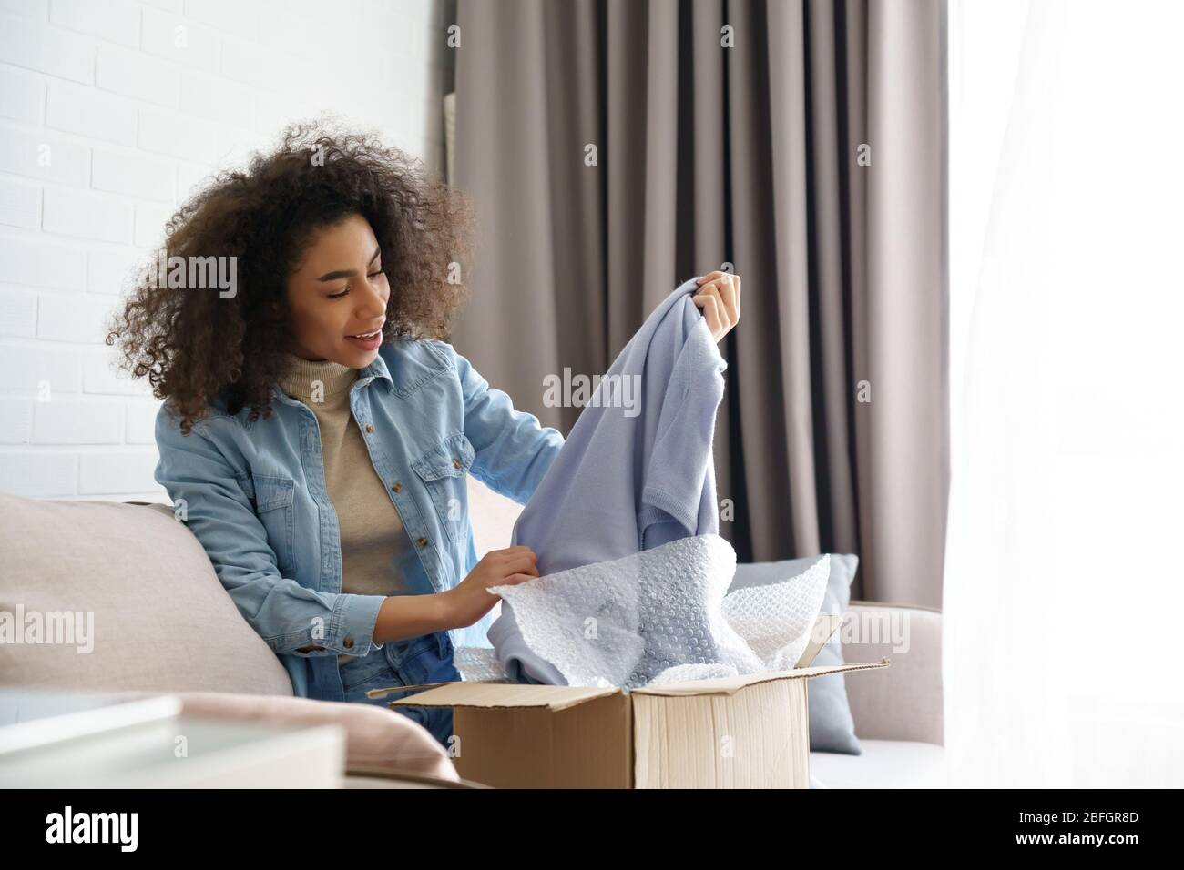 Erstaunt african junge Mädchen Kunde Auspacken Mode Lieferung box zu Hause. Stockfoto