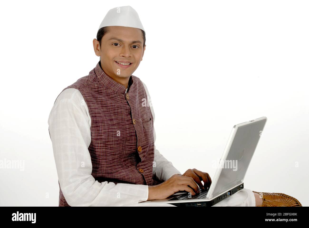 Mumbai; Maharashtra; Indien-Asien; 26. Dezember 2009 - Portrait junger gutaussehender lächelnder indischer Politiker, der mit Laptop-weißem Hintergrund arbeitet Stockfoto