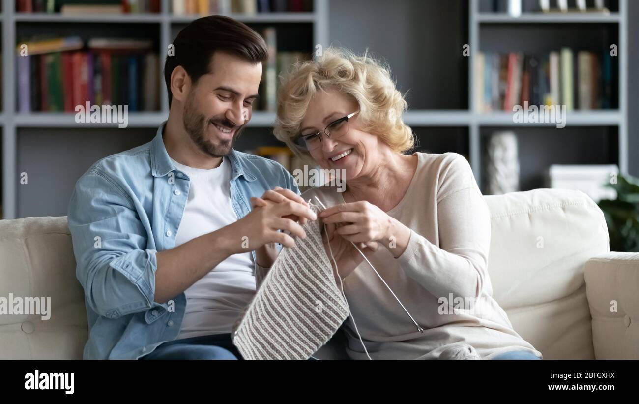 Erwachsener Sohn versuchen, gealterte Mutter zu stricken hilft ihm Stockfoto