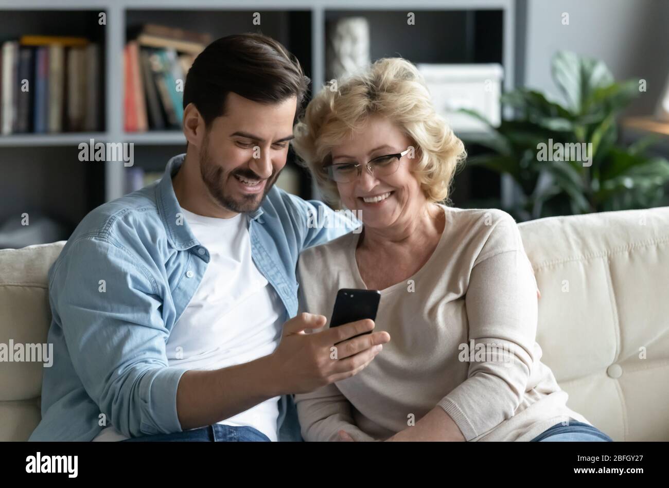 Erwachsener Sohn zeigt ältere Mutter neue Anwendung auf dem Smartphone Stockfoto