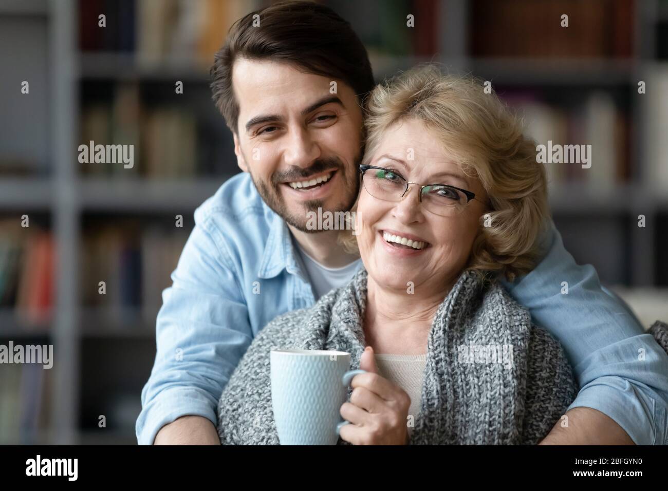 Ältere Mutter hält Tasse Tee genießt erwachsenen Sohn warme Embracement Stockfoto