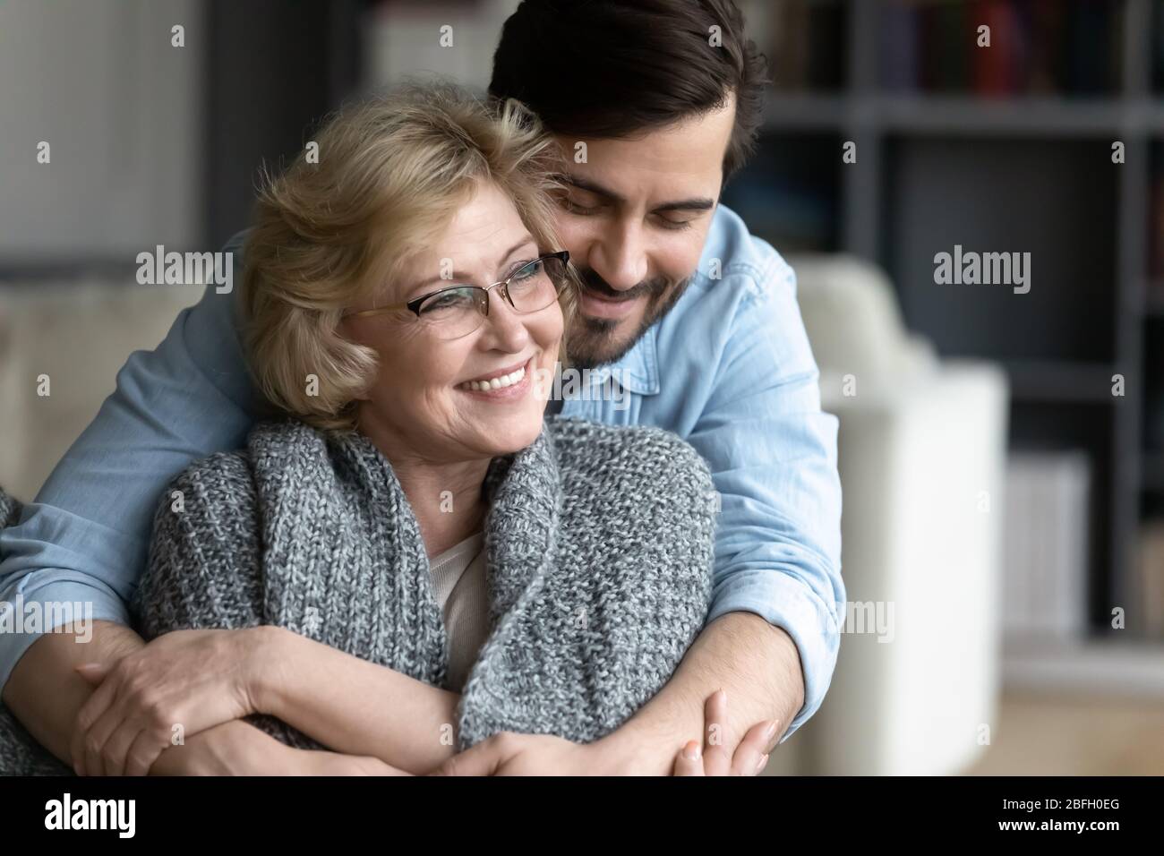 Erwachsene erwachsener Sohn umarmt von hinten ältere Mutter Stockfoto