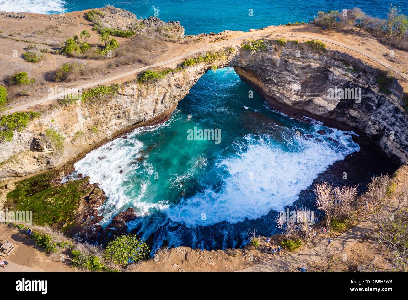 Luftaufnahme der Meereswellen, die durch einen Felsbogen in eine runde, isolierte Bucht stürzen (Broken Beach, Nusa Penida, Indonesien) Stockfoto