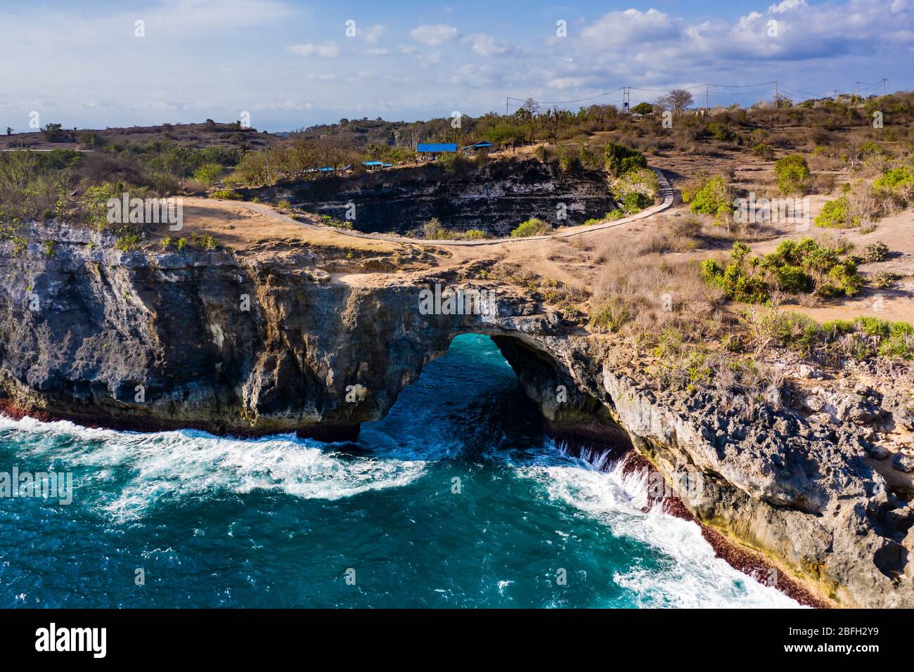 Luftaufnahme der Meereswellen, die durch einen Felsbogen in eine runde, isolierte Bucht stürzen (Broken Beach, Nusa Penida, Indonesien) Stockfoto