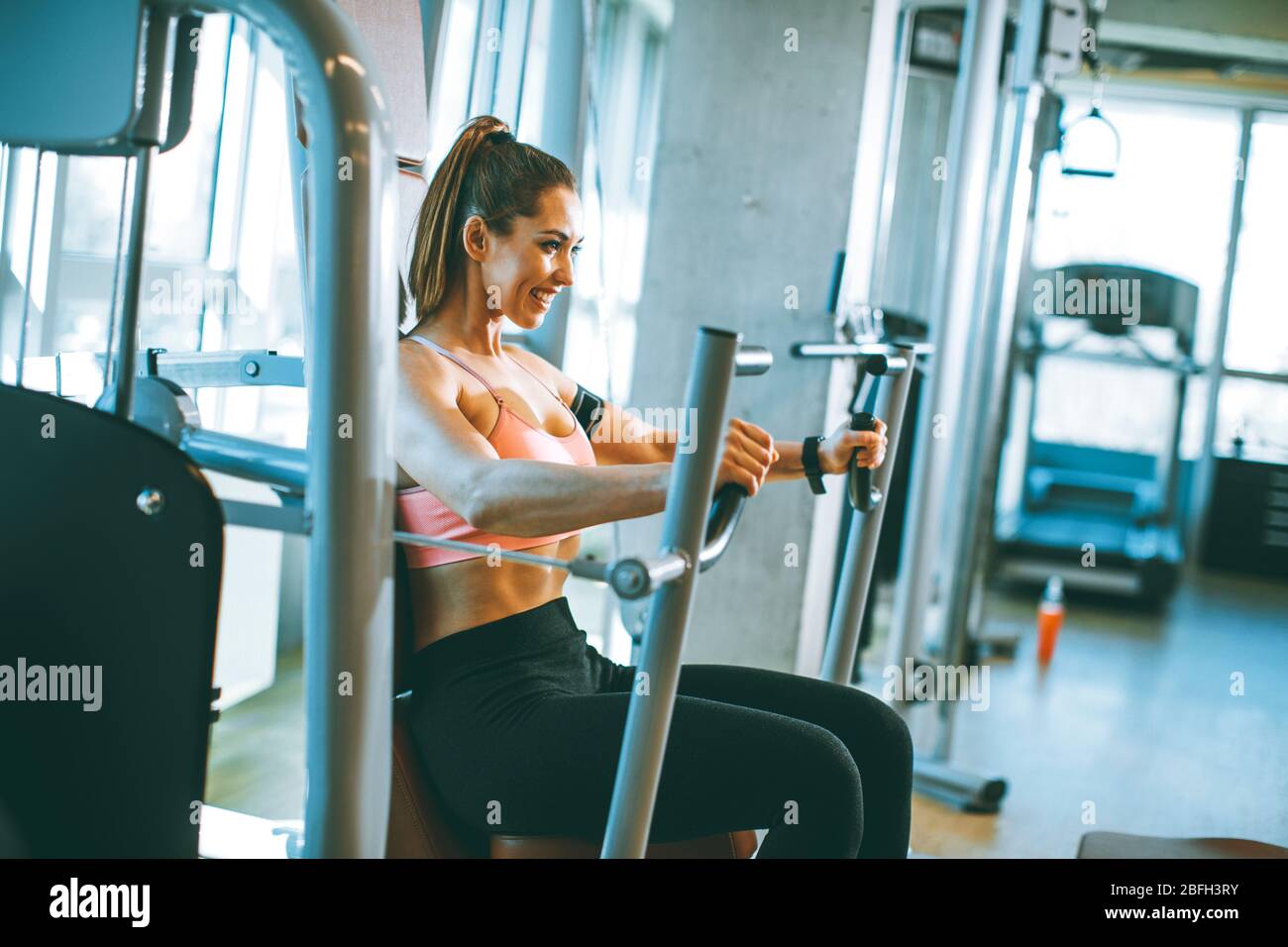 Ziemlich junge entschlossen Fitness-Frau Übungen an Brustpresse Maschine in modernen Fitnessraum Stockfoto