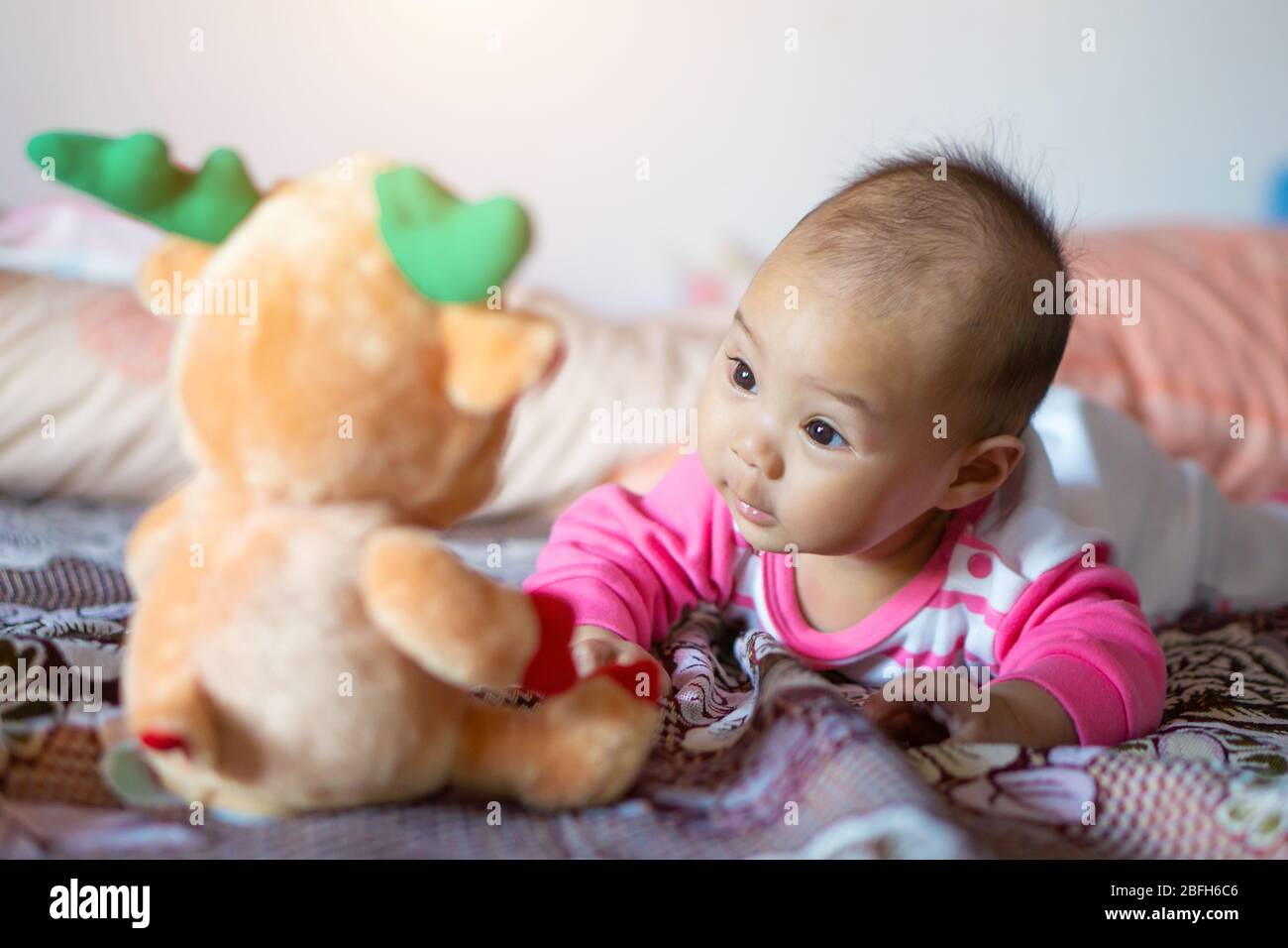 Ein 6 Monate altes asiatisches Mädchen lächelt und genießt seine Puppe. Stockfoto
