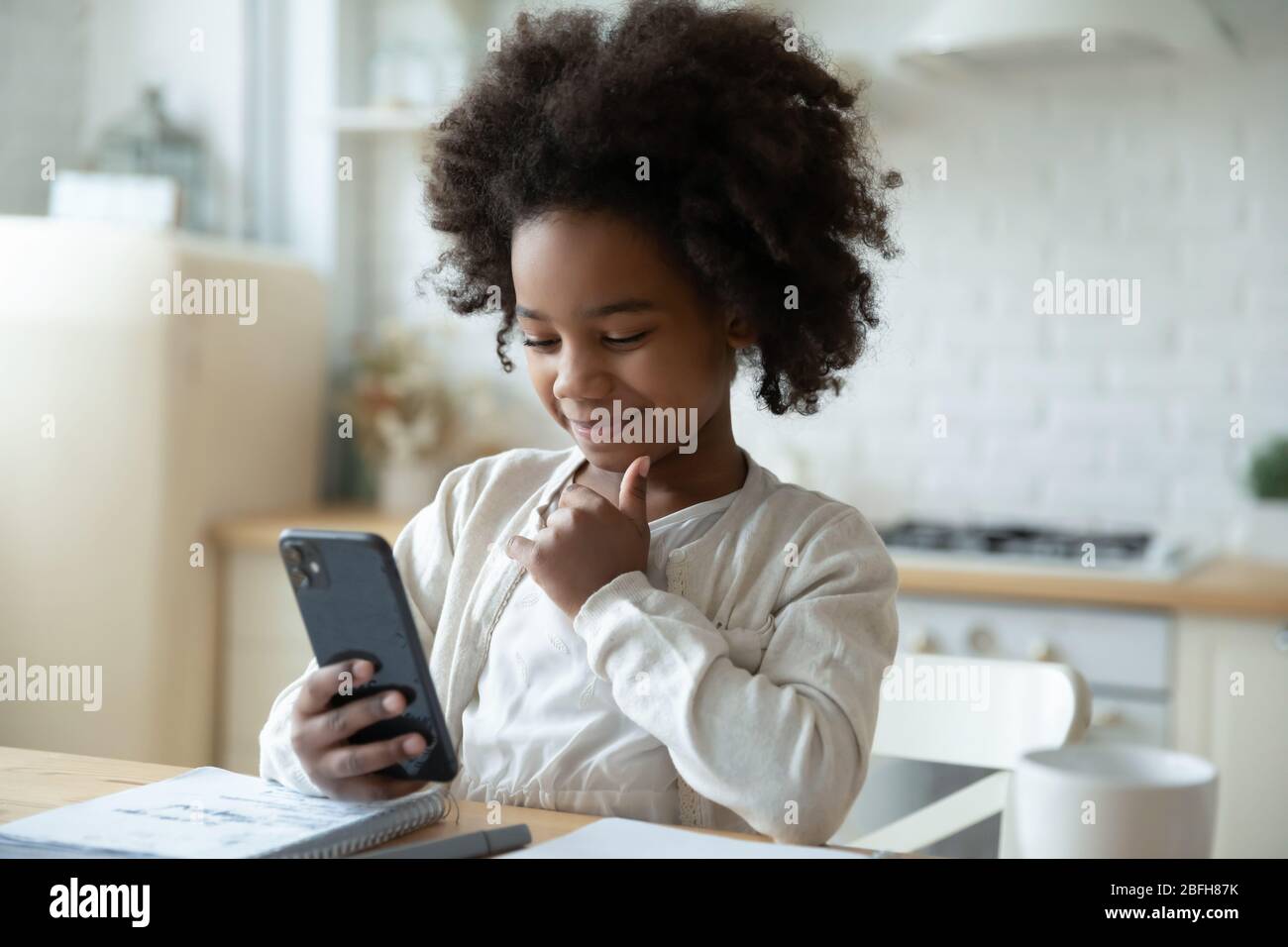 Kleine biracial Mädchen beobachten Online-Klasse auf Handy Stockfoto
