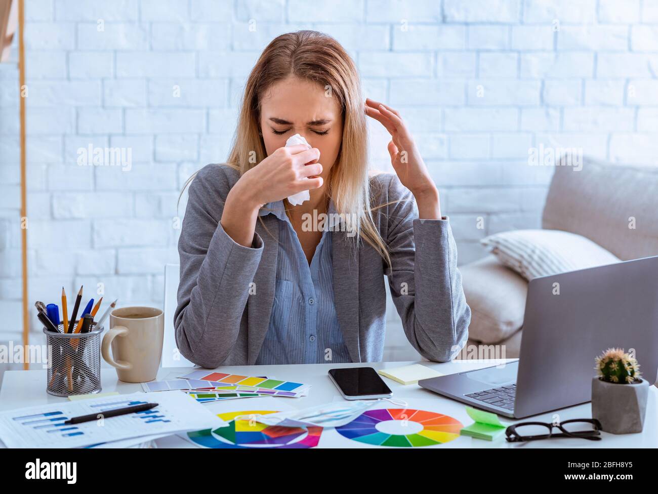 Frau, die am Arbeitsplatz die Nase mit Serviette wischt Stockfoto