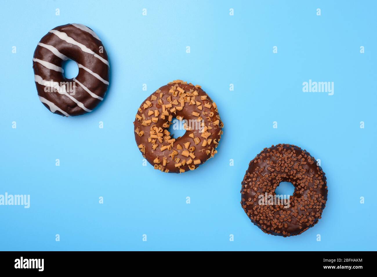 Drei leckere köstliche runde glasiert in Schokolade Creme Donuts flach liegend in Linie isoliert über Pastell Retro Sommer blauen Hintergrund Stockfoto