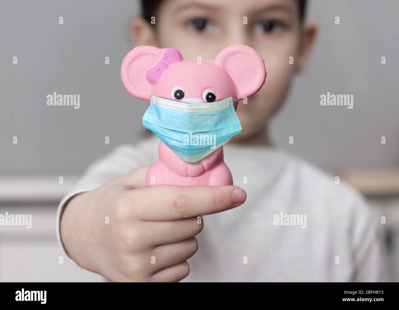Schutz gegen Corona-Virus-Konzept. Kind Mädchen halten Spielzeug mit medizinischen Maske. Stockfoto