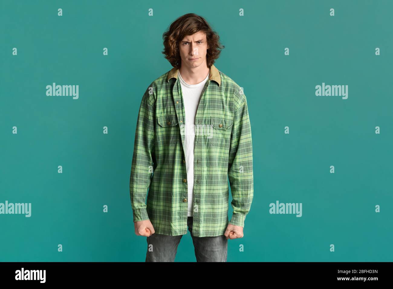 Junger Mann, der seine Fäuste in Wut zusammenklammert und auf türkisfarbenem Hintergrund die Stirn runzelt Stockfoto