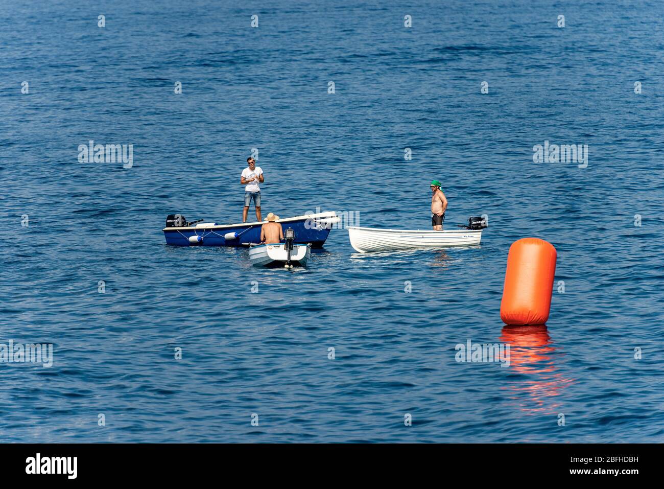 Drei Männer, jeder in seinem eigenen kleinen Boot, unterhalten sich mitten im Meer in der Nähe einer großen orangefarbenen Boje. Ligurien, Italien, Europa Stockfoto