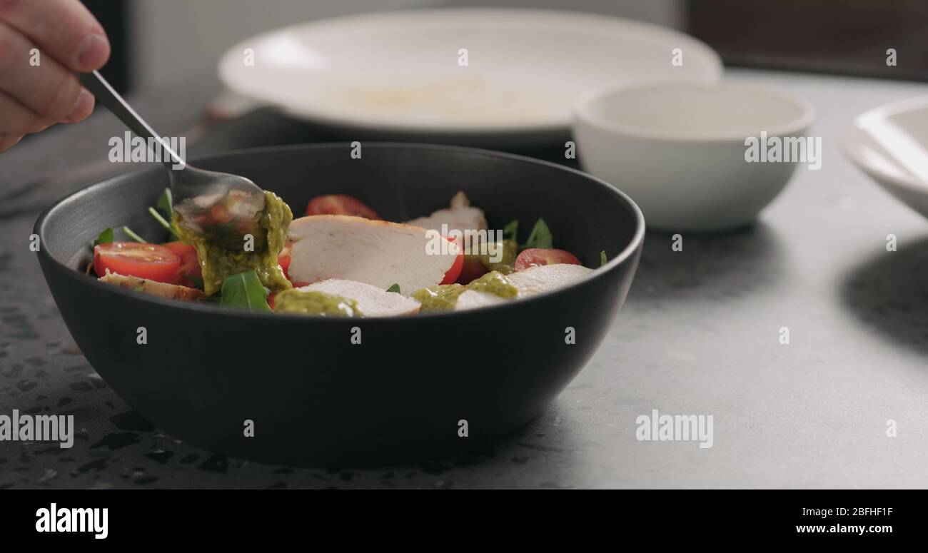 Pesto auf Salat mit Huhn, Rucola und Tomaten in schwarzer Schüssel geben Stockfoto