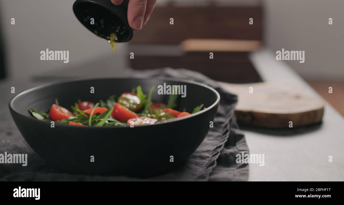 Pesto auf Salat mit Huhn, Rucola und Tomaten in schwarzer Schüssel geben Stockfoto