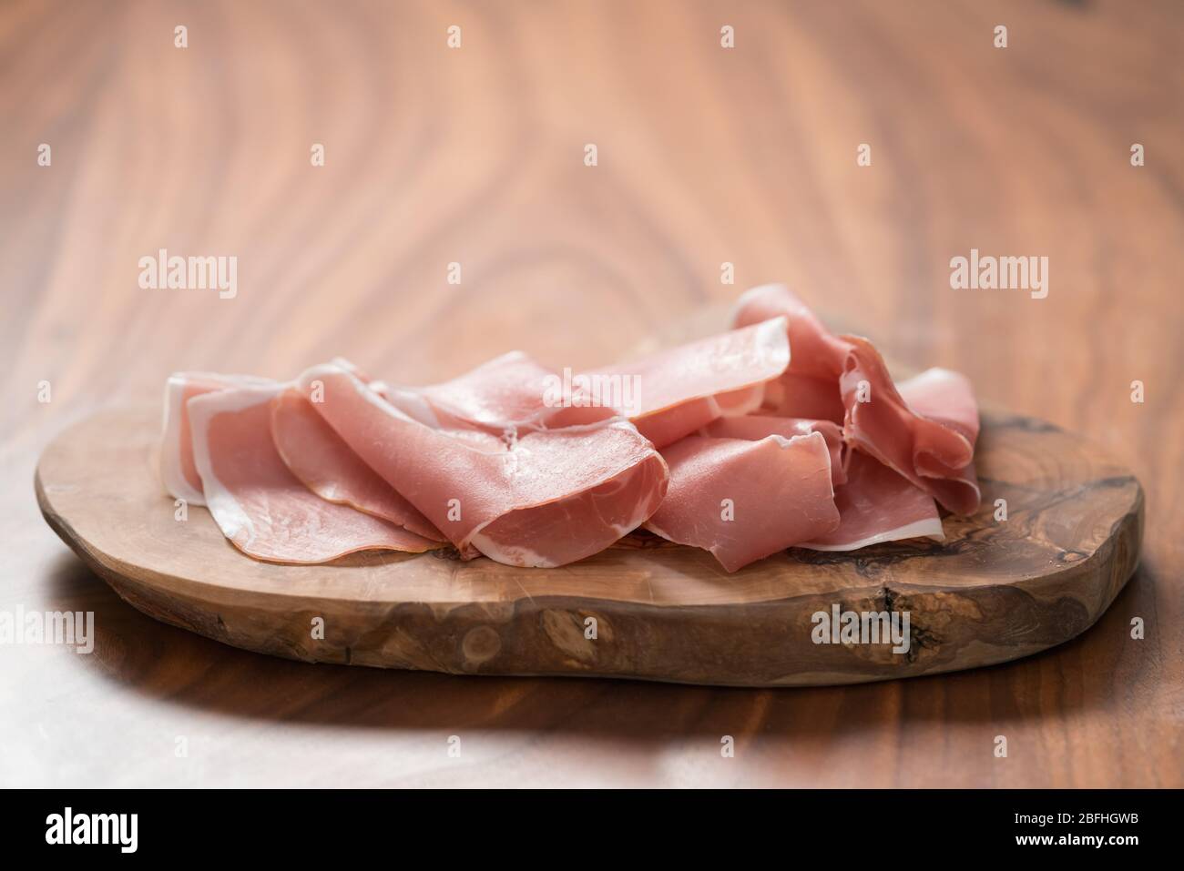 Dünne italienische Prosciutto-Scheiben auf Olivenholzplatte auf Walnuss Tabelle Stockfoto