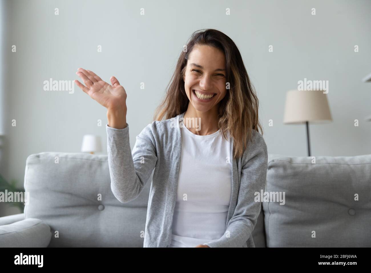 Glückliche junge Frau winkt Hand, Blick auf die Kamera Stockfoto