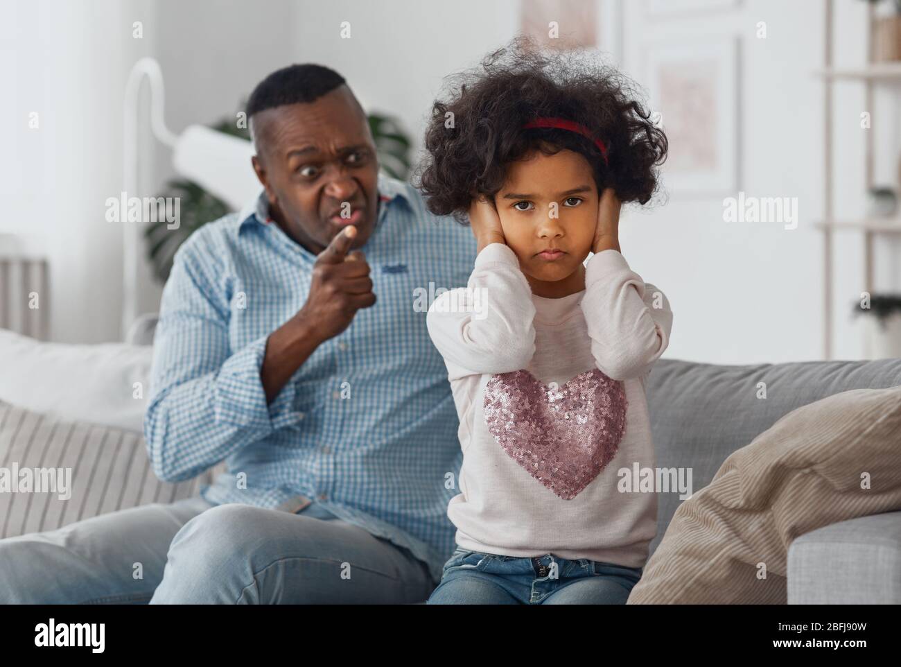 Wütend afroamerikanischen Großvater schreit seine Enkelin zu Hause, konzentrieren sich auf Kind Ohren schließen Stockfoto