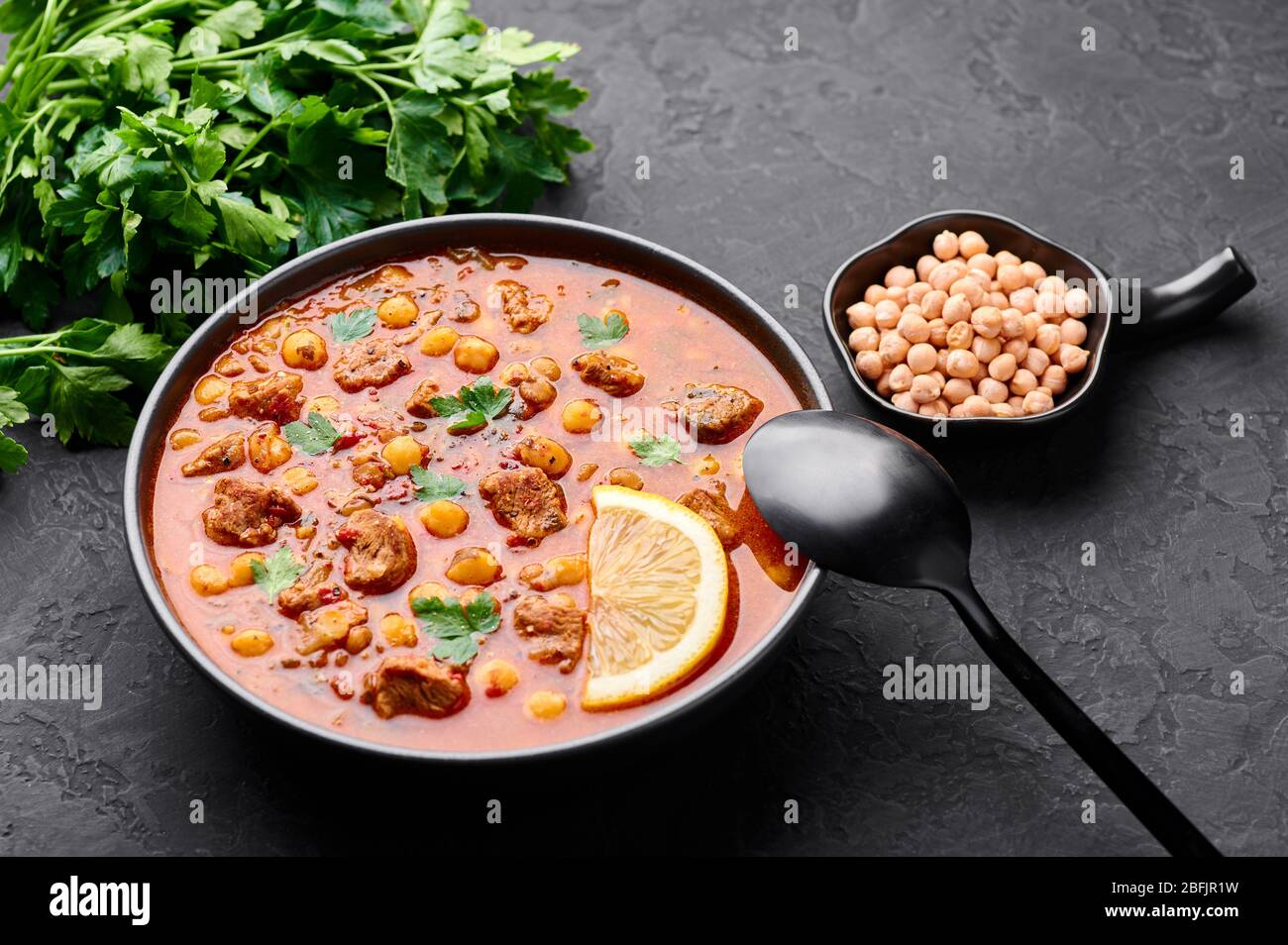 Marokkanische Harira Suppe in schwarzer Schüssel auf dunklem Schiefer-Background. Harira ist marokkanische Küche Gericht mit Lamm oder Rindfleisch, Kichererbsen, Linsen, Tomaten und Stockfoto