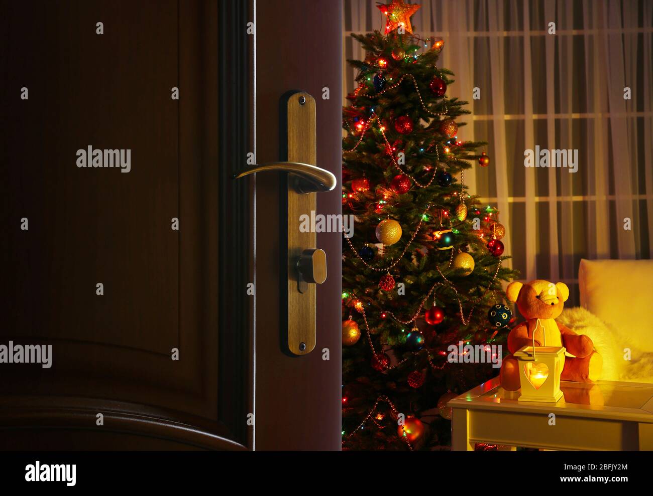 Offene Tür mit geschmücktem Weihnachtsbaum im Zimmer Stockfoto