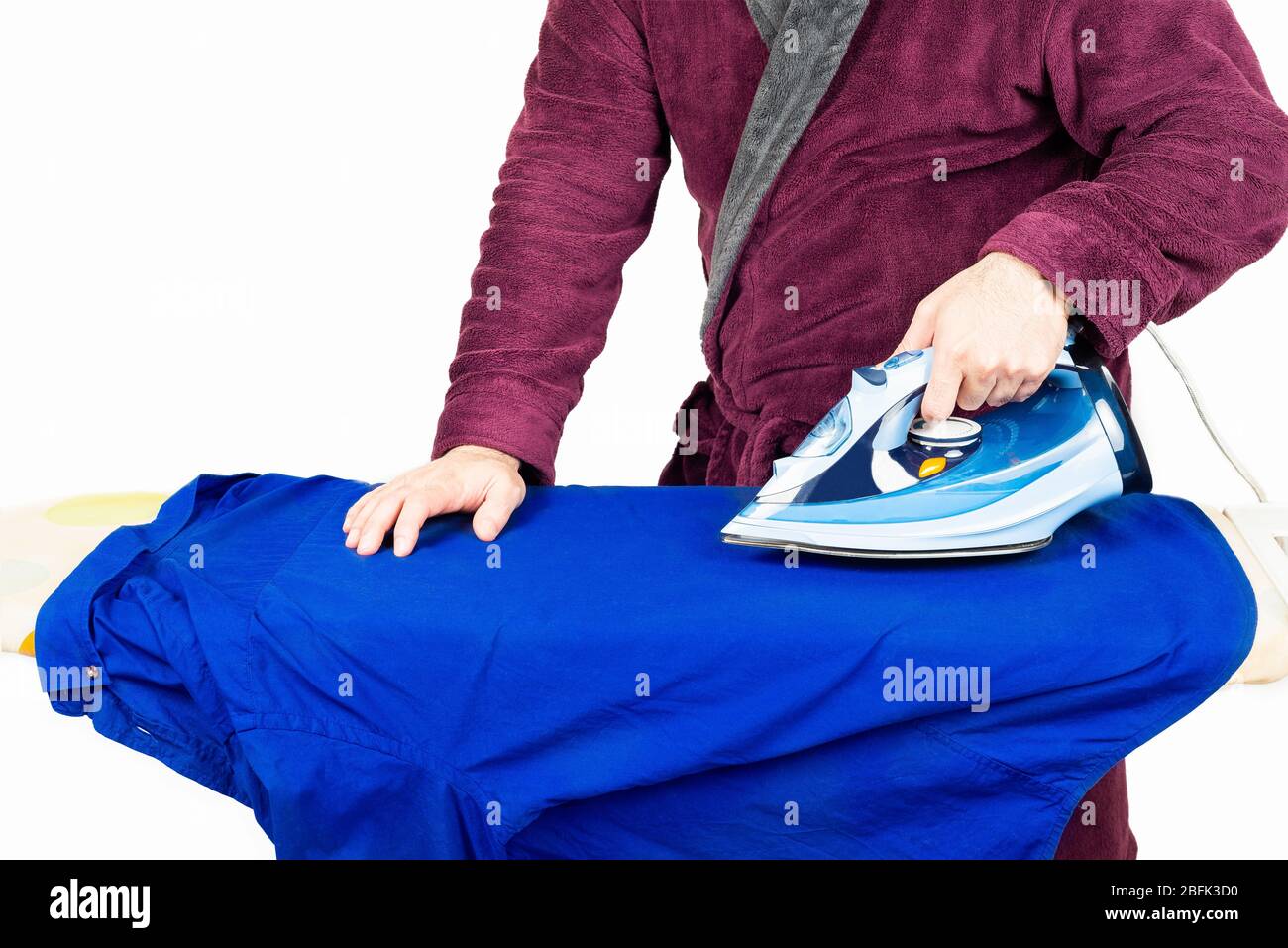 Mann in einem roten Gewand bügelt ein blaues Hemd Stockfoto