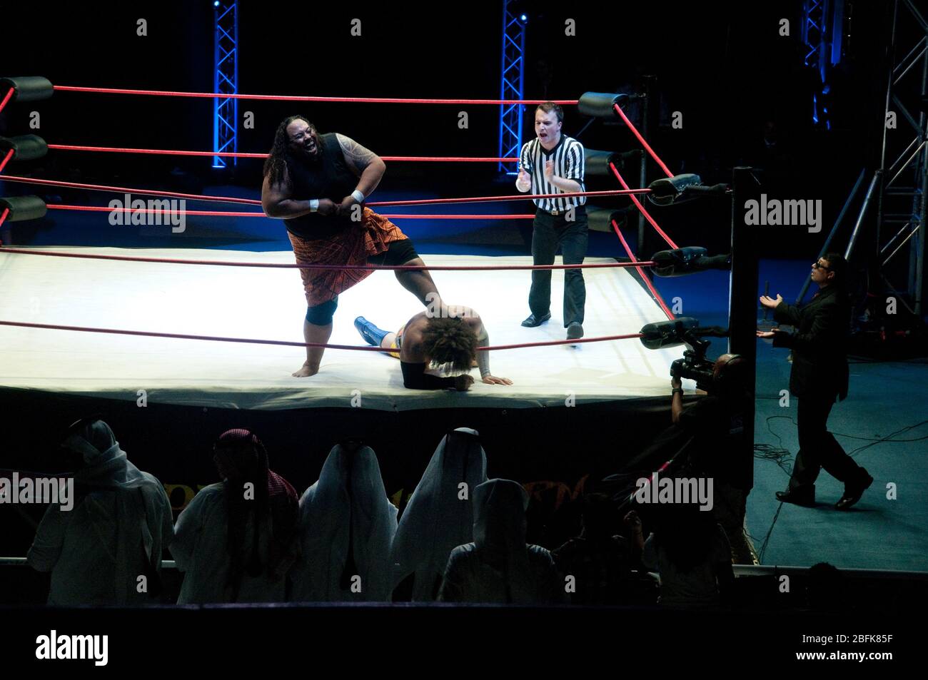 Zwei professionelle Ringer kämpfen im Ring neben einem Schiedsrichter und einem Manager bei einem Live-Outdoor-Wrestling-Match in der Stadt Doha in Katar. Stockfoto